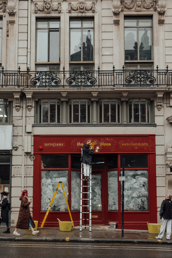  The Eye Place, Fleet Street red shop front. Woman on ladder painting the shop sign. OPTICIANS AUDIOLOGISTS.